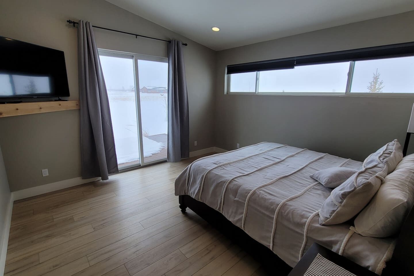A bedroom with a bed, a TV mounted on the wall, and a large window.