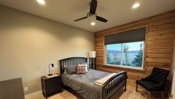 A bedroom with a bed, a nightstand, a chair, a ceiling fan, and a window with a view. - Indoor/Outdoor Living with 4-Peak Teton View (Driggs)