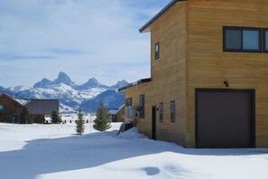 A wooden building with a garage, surrounded by snow and mountains in the background.