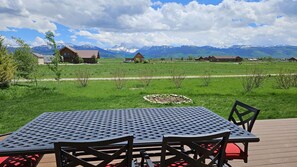 Une table et des chaises sur une terrasse extérieure, avec vue sur un champ verdoyant et des montagnes en arrière-plan.