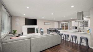 Una sala de estar moderna con un sofá seccional, una chimenea, un comedor con mesa y sillas, y una cocina con barra.