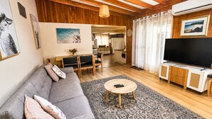 Una sala de estar moderna con un sofá, una mesa de centro y un televisor. Se aprecia un comedor con una mesa y sillas, y una cocina al fondo.
