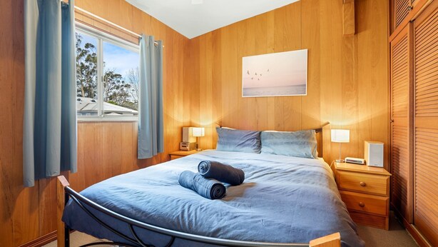 Un dormitorio con una cama, dos mesitas de noche, una ventana con cortinas y un cuadro en la pared.