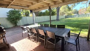 Un patio cubierto con mesa y sillas, una parrilla y vistas a un jardín césped.