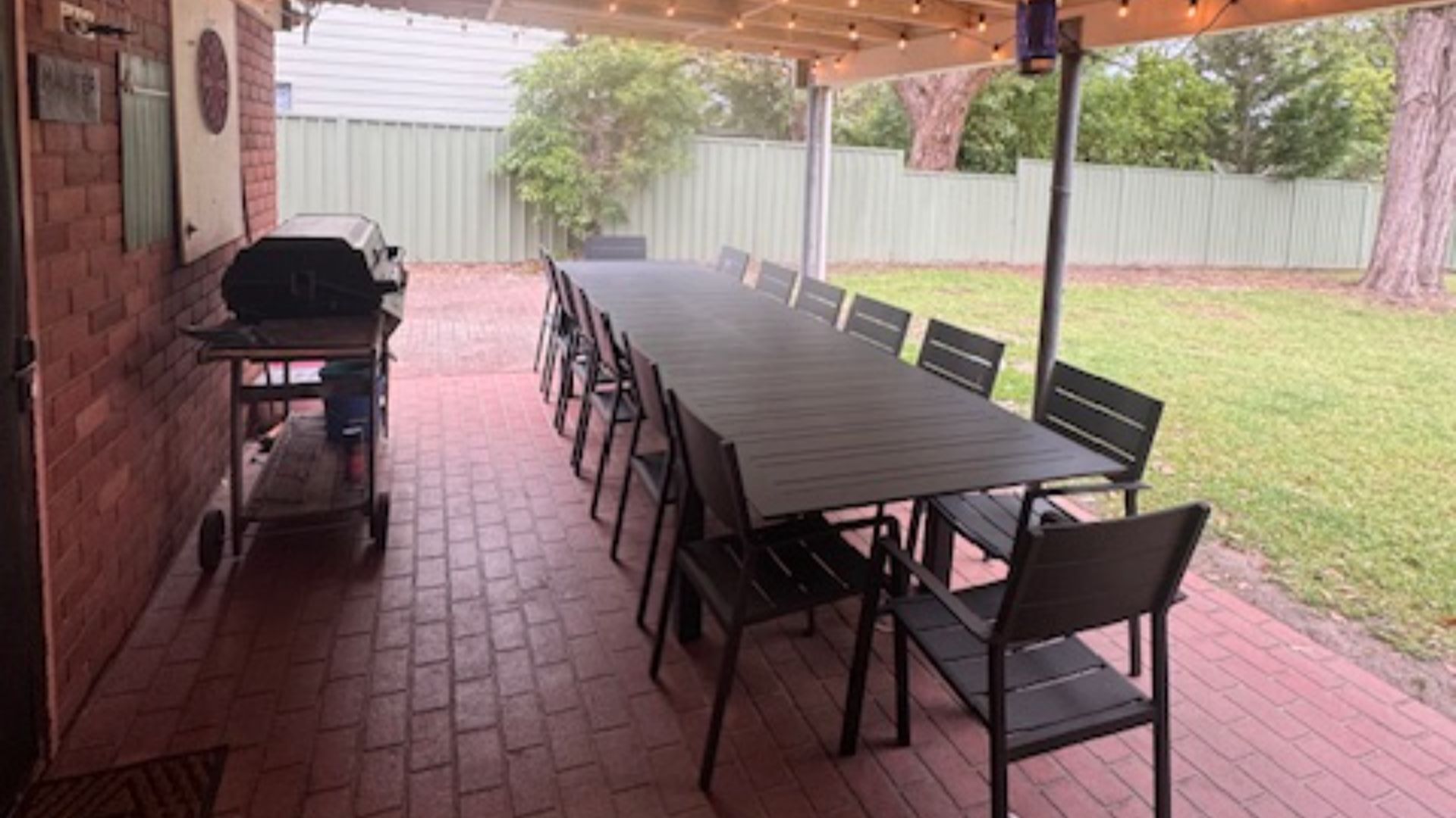 An outdoor patio with a brick floor, a long table, and chairs.