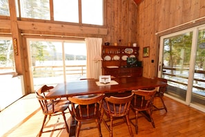 A wooden dining room with a large table and chairs, a window with curtains, and a view of a snowy landscape.
