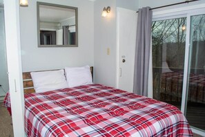 A bedroom with a bed, a mirror, a sliding glass door, and a view of the outdoors.
