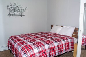 A single bed with a plaid bedspread, a wooden headboard, and a wall decoration of abstract trees.