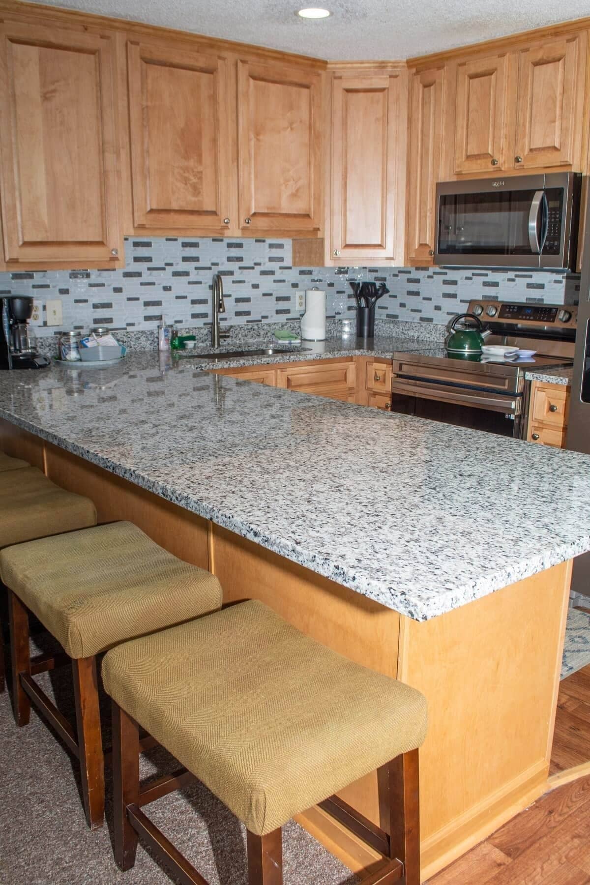 Una cocina con armarios de madera, encimera de granito, microondas de acero inoxidable y hervidor verde.