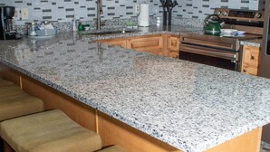 Une cuisine avec des meubles en bois, un plan de travail en granit, un four à micro-ondes en acier inoxydable et une bouilloire verte.