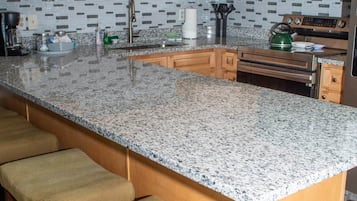 Una cocina con armarios de madera, encimera de granito, microondas de acero inoxidable y hervidor verde.