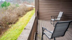 A wooden deck with two chairs and a view of a grassy area with bushes and trees. - Winterplace E102 Ski in Ski out First Floor (Ghent)