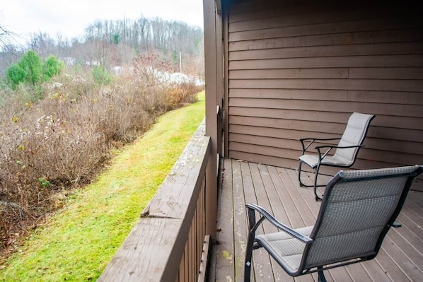 A wooden deck with two chairs and a view of a grassy area with bushes and trees.