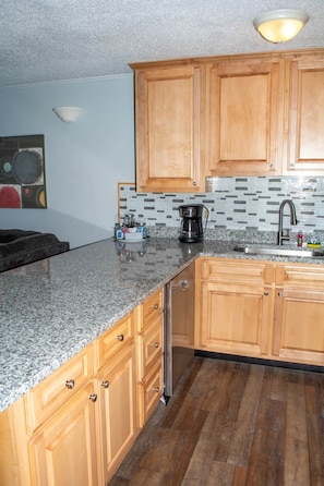 A kitchen with wooden cabinets, a granite countertop, a coffee maker, and a sink. - Winterplace E103 Ski in Ski out condo First floor (Ghent)