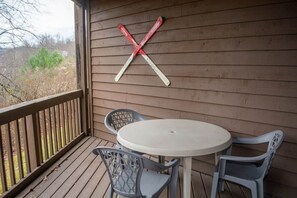 A wooden deck with a round table and two chairs, a wooden railing, and a red and white X-shaped decoration on the wall. - Winterplace E103 Ski in Ski out condo First floor (Ghent)