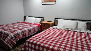 A room with two beds, each with a checkered bedspread, a nightstand with a drawer, and a wall-mounted light switch. - Winterplace E103 Ski in Ski out condo First floor (Ghent)