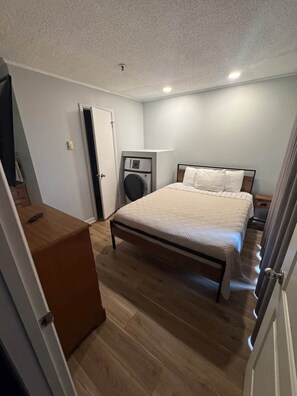 A bedroom with a bed, a washing machine, a desk, and a door.