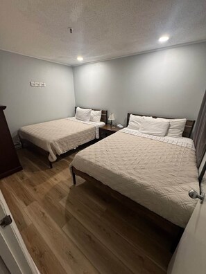 Une chambre d’hôtel avec deux lits simples, un plancher en bois, une table de chevet avec une lampe et une prise électrique au mur.