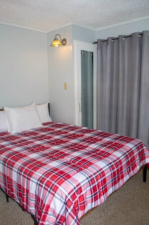 A bedroom with a bed, white pillows, a red and white checkered bedspread, a wall-mounted light fixture, and a door with a gray curtain.