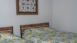 Une chambre avec deux lits simples, une tête de lit en bois, un mur sobre et un élément décoratif en métal au-dessus des lits.