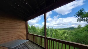 Eine Holzterrasse mit Tisch und Geländer, mit Blick auf eine grüne Landschaft.