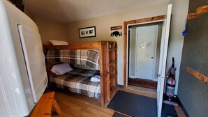 Ein kleines Zimmer mit Bett, Sitzbank, Tür und Kühlschrank.