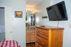 A bedroom with a bed, wooden dresser, TV, and a bathroom with a sink and mirror. - Winterplace D104 Ski in Ski out condo First floor (Ghent)