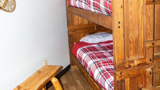 Un lit superposé avec une structure en bois, un banc et une étagère murale sur laquelle est posée une image.