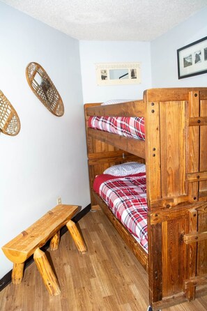 A bunk bed with a wooden frame, a bench, and a wall-mounted shelf with a picture.