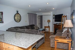 A living room with a sofa, a coffee table, a lamp, a clock, and a television. - Winterplace D104 Ski in Ski out condo First floor (Ghent)