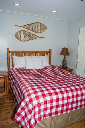 A bedroom with a wooden bed, checkered bedding, a nightstand, a lamp, and wall decorations. - Winterplace D104 Ski in Ski out condo First floor (Ghent)