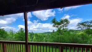 Une terrasse en bois offrant une vue sur un paysage verdoyant et des arbres sous un ciel dégagé.