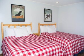 A room with two beds, each with a checkered red and white bedspread, wooden headboards, white pillows, and a framed poster of a black dog on the wall. - Winterplace D104 Ski in Ski out condo First floor (Ghent)
