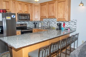 A kitchen with wooden cabinets, a granite countertop, a stainless steel refrigerator, a microwave, and a stove. - Winterplace D104 Ski in Ski out condo First floor (Ghent)