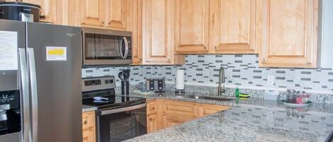 A kitchen with wooden cabinets, granite countertops, stainless steel appliances, and a tiled backsplash.