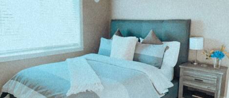 A bedroom with a sloped ceiling, a bed with a blue and white bedspread, a nightstand with a lamp, and a window with blinds.