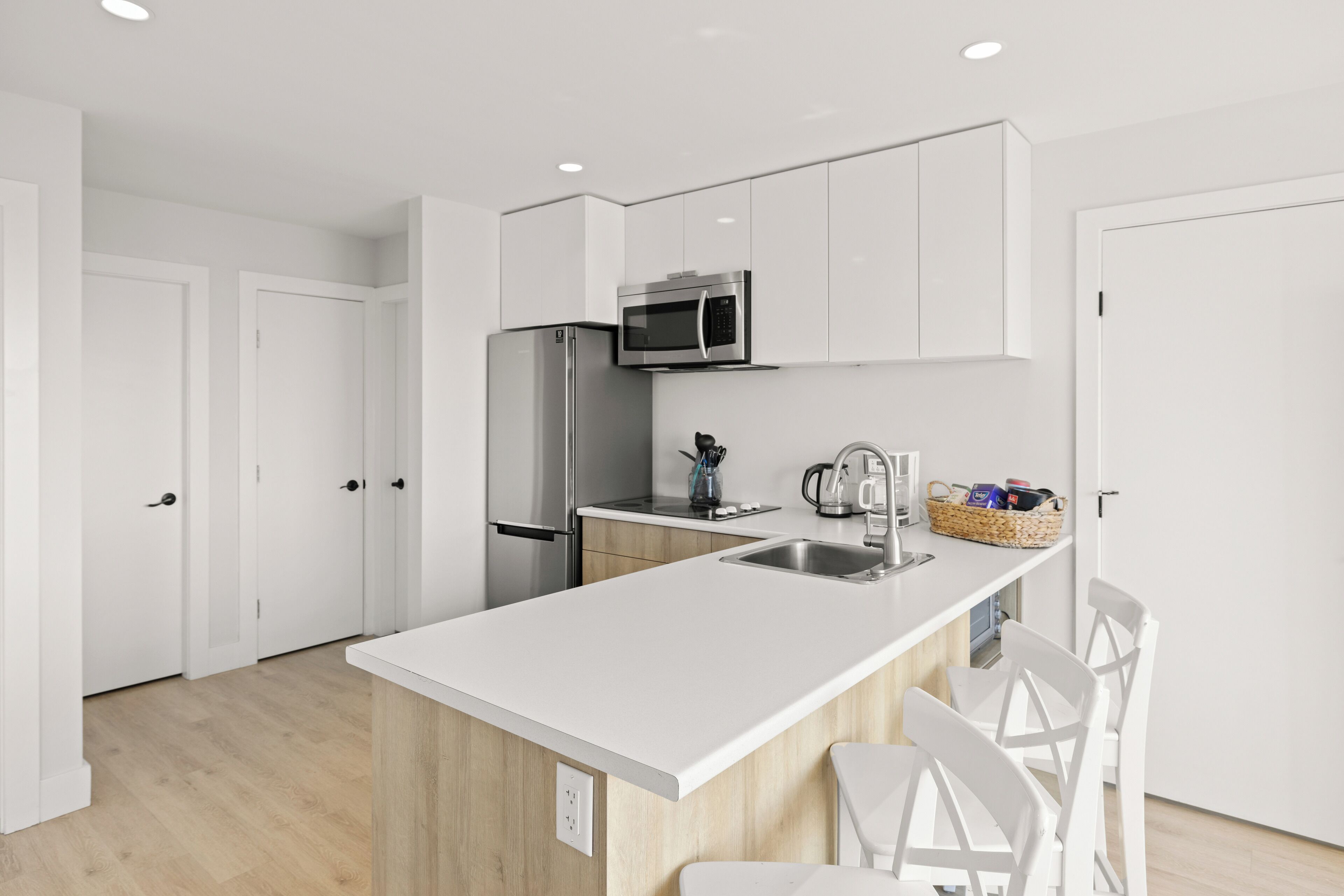A modern kitchen with white cabinetry, stainless steel appliances, and a white countertop.
