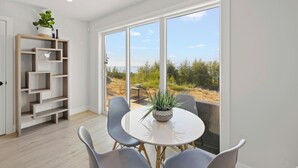 A modern room with a round table, four chairs, a potted plant, and a wooden shelving unit. - The Owl’s Nest | Panoramic Ocean View Retreat (Sooke)