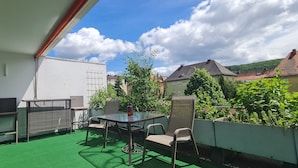 A balcony with a green artificial turf, a table, two chairs, and a small plant. - Studio Apartment Terrassengarten - Bad Kissingen (Bad Kissingen)