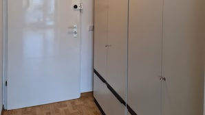 A hallway with a white door, wooden flooring, and a wardrobe with multiple doors. - Studio Apartment Terrassengarten - Bad Kissingen (Bad Kissingen)