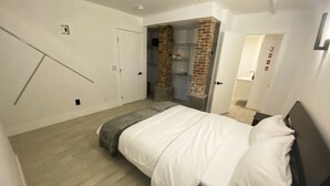 A bedroom with a bed, a brick wall, and a door leading to a bathroom. - Ultra cool new modern flat (Portland)