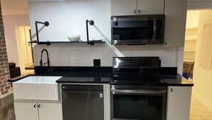 A modern kitchen with white cabinetry, a black countertop, a built-in dishwasher, a stove, and a microwave. - Ultra cool new modern flat (Portland)