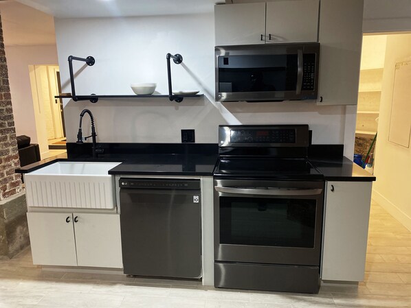 Een moderne keuken met witte kasten, een zwart aanrecht, een ingebouwde vaatwasser, een fornuis en een magnetron.