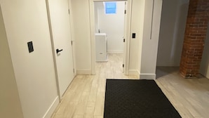 Un pasillo con alfombra negra, puertas blancas y una lavandería visible al fondo.