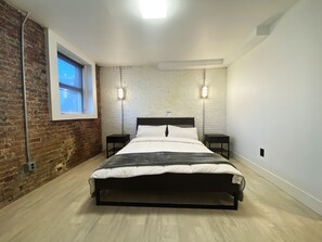 A modern bedroom with a brick wall, a large bed, two bedside tables, and a window. - Ultra cool new modern flat (Portland)