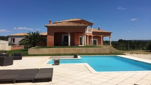 Une maison à deux étages avec une piscine, du mobilier d’extérieur et un ciel d’un bleu éclatant.