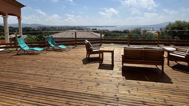 Une terrasse en bois avec des chaises longues et une table, offrant une vue panoramique sur un paysage magnifique, avec des montagnes et une étendue d’eau.