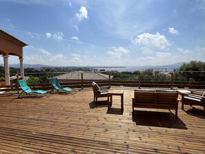 Een houten terras met lounge stoelen en een tafel, met uitzicht op een schilderachtige omgeving met bergen en een waterpartij.