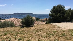 Une vue sur la côte, avec des bâtiments aux toits de tuiles rouges, une zone sablonneuse et un ciel bleu dégagé.