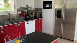 Une cuisine moderne avec un plan de travail noir, des armoires rouges, des appareils en acier inoxydable et une fenêtre donnant sur un paysage verdoyant.